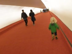 Fiona and her green raincoat stand out against the red carpeting and white walls of one of the two tube-shaped corridors that connected the head house to the original gates. The southern tube dates from the original 1962 Saarinen structure while the northern one, seen in this photo, was added in 1969 as part of Flight Wing One by architects Kevin Roche and John Dinkeloo.